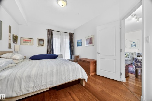 Spacious room featuring wood-finish flooring, a contemporary ceiling light fixture, a window with curtain rods, and a solid core door - 304 10116 80 Avenue, Edmonton, AB 