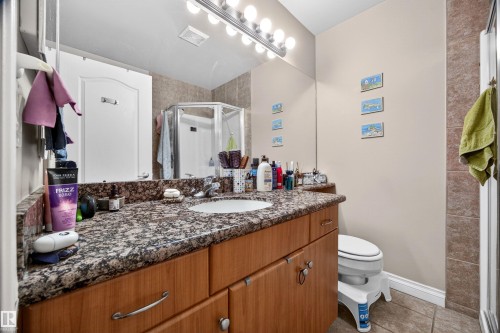 Bathroom featuring a wood-finish vanity with a speckled countertop, a large mirror, a chrome-finish light fixture, and a shower enclosure - 304 10116 80 Avenue, Edmonton, AB 