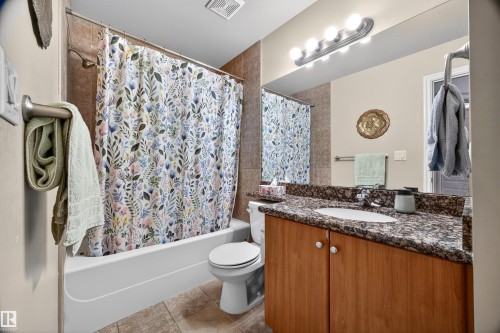Full bathroom featuring a single vanity with wood-finish cabinetry, a white basin sink, and a speckled countertop - 304 10116 80 Avenue, Edmonton, AB 