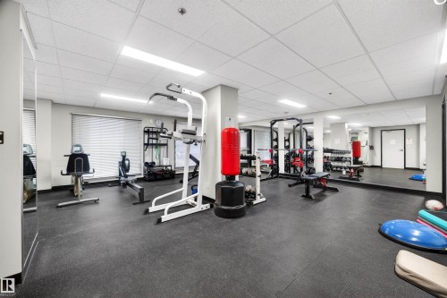 Fitness room featuring rubberized flooring, mirrored walls, drop ceiling, and recessed lighting - 304 10116 80 Avenue, Edmonton, AB 