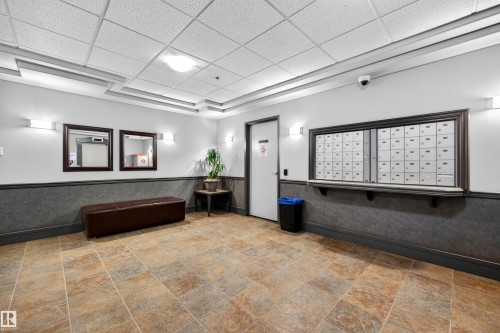 Entryway featuring neutral-toned tile flooring, wainscoting, wall sconces, a dropped ceiling with recessed lighting, and a mail station - 304 10116 80 Avenue, Edmonton, AB 