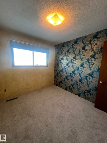 Room featuring textured wallpaper, neutral carpeting, and a single window with blinds - 15003 81 Street, Edmonton, AB 