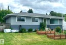 Ranch-style exterior featuring a vibrant green entry door, white trim windows, and two raised garden beds - 15003 81 Street, Edmonton, AB 