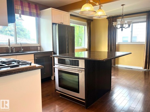 Kitchen featuring dark wood-finish flooring, white cabinetry, dark countertops, and stainless steel appliances including a built-in oven, refrigerator, and dishwasher - 15003 81 Street, Edmonton, AB 