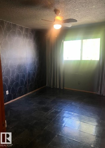 Spacious room featuring dark tile flooring, a window with drapery, and a ceiling fan with integrated lighting - 15003 81 Street, Edmonton, AB 