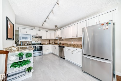 Kitchen featuring white cabinetry, stainless steel appliances, granite countertops, a tiled backsplash, and light-toned flooring - 50 303 Twin Brooks Drive Nw, Edmonton, AB 