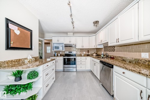 Kitchen featuring wood-finish flooring, white cabinetry, granite-style countertops, stainless steel appliances, and a tile backsplash - 50 303 Twin Brooks Drive Nw, Edmonton, AB 