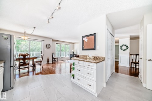 Kitchen and living area featuring light gray tile flooring, track lighting, white cabinetry with a stone-finish countertop, and wood-finish flooring extending into the main living space - 50 303 Twin Brooks Drive Nw, Edmonton, AB 