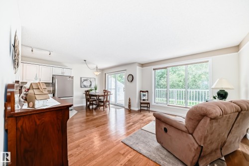 Open-concept living area featuring wood-finish flooring, white kitchen cabinetry, stainless steel appliances, and a sliding glass door to a balcony - 50 303 Twin Brooks Drive Nw, Edmonton, AB 