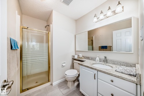 Bathroom featuring a granite countertop vanity with integrated sink, white cabinetry, and a full-width mirror - 50 303 Twin Brooks Drive Nw, Edmonton, AB 