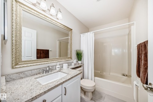 Bathroom featuring a full-width vanity with white cabinetry, a light-toned speckled countertop, an undermount sink with a chrome faucet, and a large ornate framed mirror - 50 303 Twin Brooks Drive Nw, Edmonton, AB 