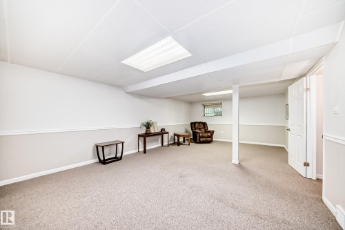 Spacious carpeted room featuring a drop ceiling with integrated lighting, two-tone painted walls with chair rail molding, and a white paneled door - 50 303 Twin Brooks Drive Nw, Edmonton, AB 
