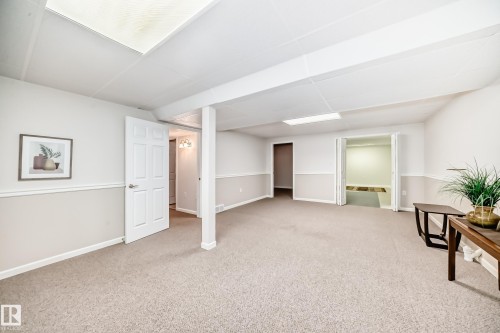 Expansive carpeted room featuring a drop ceiling with recessed lighting, two-tone painted walls with chair rail molding, and multiple doorways for access - 50 303 Twin Brooks Drive Nw, Edmonton, AB 