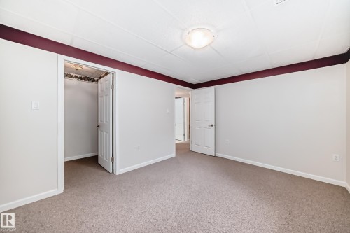 Carpeted room featuring white walls with a dark accent border, a white paneled door, and a flush mount ceiling light fixture - 50 303 Twin Brooks Drive Nw, Edmonton, AB 