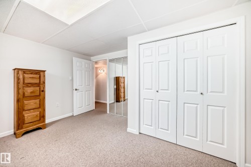 Wall-to-wall carpeting with bi-fold closet doors featuring panel detailing, white trim, and a drop ceiling - 50 303 Twin Brooks Drive Nw, Edmonton, AB 