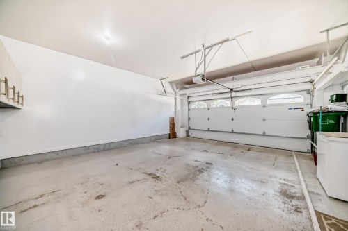 Spacious garage featuring a sectional overhead door with arched window inserts, built-in overhead storage racks, integrated lighting, and wall-mounted cabinetry with brushed nickel pulls - 50 303 Twin Brooks Drive Nw, Edmonton, AB 