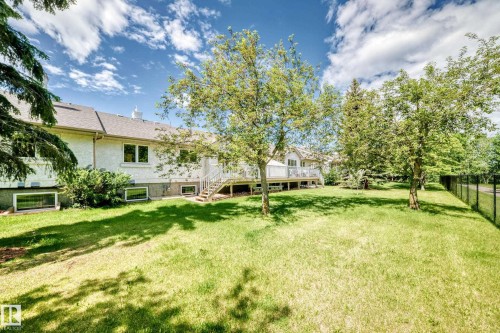 Spacious backyard featuring a manicured lawn, established trees, and a black chain-link fence - 50 303 Twin Brooks Drive Nw, Edmonton, AB 