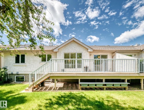 Rear exterior featuring a spacious elevated deck with railing, direct stair access to the lawn, multiple windows, and a stucco finish - 50 303 Twin Brooks Drive Nw, Edmonton, AB 