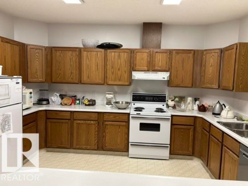 Kitchen featuring extensive wood-finish cabinetry, white countertops, a white electric range, and a double-basin stainless steel sink - 50 303 Twin Brooks Drive Nw, Edmonton, AB 