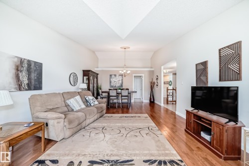 Open-concept living space featuring wood-finish flooring, vaulted ceilings, and a dining area with a chandelier - 50 303 Twin Brooks Drive Nw, Edmonton, AB 