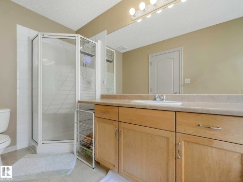 Bathroom featuring a corner shower enclosure with clear glass, light wood-finish cabinetry, a single basin sink, and a large wall-mounted mirror - 1116 Lincoln Crescent, Edmonton, AB - Indoor Photo Showing Bathroom