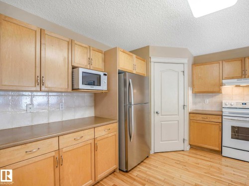 Kitchen featuring light wood cabinetry, white tile backsplash, light-toned countertops, wood-finish flooring, and a stainless steel refrigerator - 1116 Lincoln Crescent, Edmonton, AB - Indoor Photo Showing Kitchen