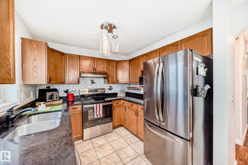 Kitchen featuring wood cabinetry, stainless steel appliances, dark countertops, a tiled backsplash, and tile flooring - 8 Campbell Court, Leduc, AB 