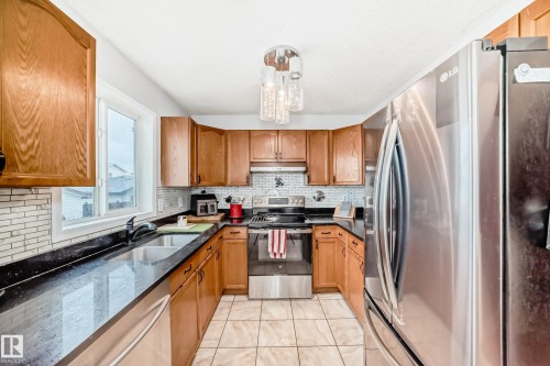 U-shaped kitchen featuring wood-finish cabinetry, dark countertops, a mosaic tile backsplash, and stainless steel appliances - 8 Campbell Court, Leduc, AB 