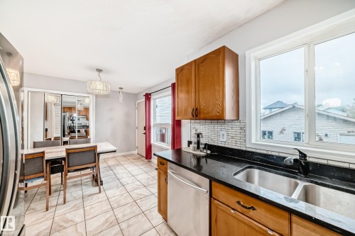 Kitchen with wood-finish cabinetry, black countertops, and a subway tile backsplash - 8 Campbell Court, Leduc, AB 