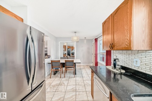 Kitchen featuring wood-finish cabinetry, a subway tile backsplash, and dark speckled countertops - 8 Campbell Court, Leduc, AB 