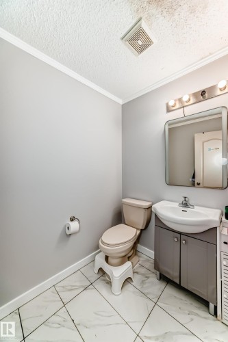 Bathroom featuring patterned tile flooring, a built-in vanity with a white sink, a wall-mounted mirror, and a multi-bulb light fixture - 8 Campbell Court, Leduc, AB 