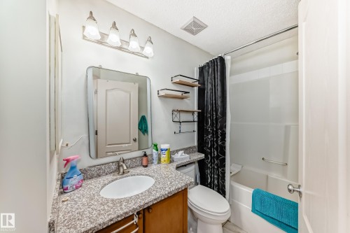 Bathroom featuring a granite-finish countertop, single basin sink, wood-finish vanity, and a full bathtub with shower - 8 Campbell Court, Leduc, AB 