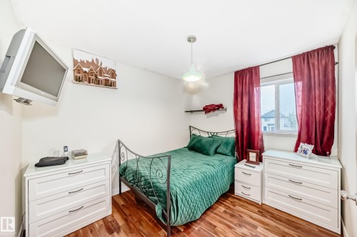 Wood-finish flooring provides a warm foundation for this bright room, featuring a large window, a ceiling-mounted light fixture, and white walls - 8 Campbell Court, Leduc, AB 