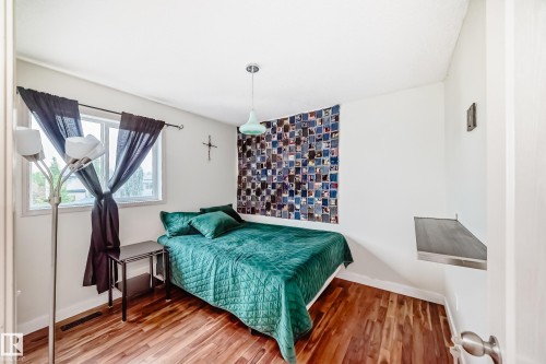 Bedroom featuring wood-finish flooring, a window with white trim, white walls, a mounted wall shelf, and a light fixture - 8 Campbell Court, Leduc, AB 