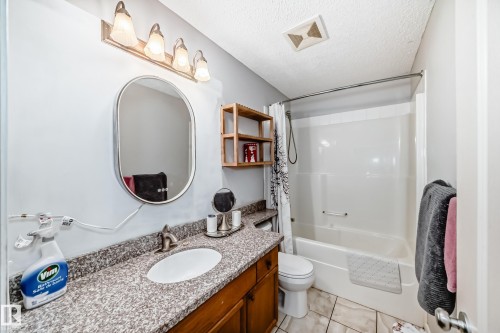 Bathroom featuring a built-in tub with shower, a vanity with a countertop and undermount sink, a wall-mounted mirror, and tile flooring - 8 Campbell Court, Leduc, AB 