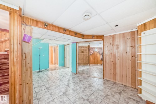 Spacious room featuring tile flooring, wood paneling, mirrored closet doors, a drop ceiling, and built-in shelving - 8 Campbell Court, Leduc, AB 