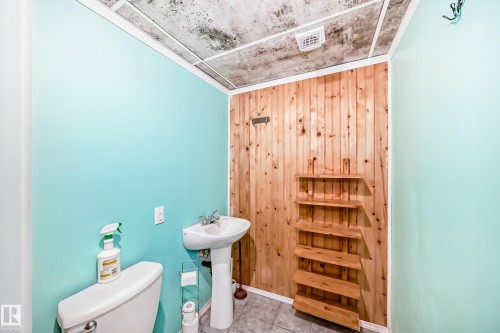Pedestal sink with chrome fixtures, wood-paneled accent wall, light blue painted walls, and tile flooring - 8 Campbell Court, Leduc, AB 