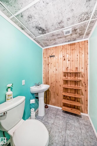 Pedestal sink with chrome faucet, light wood-paneled wall, light blue painted walls, and grey tile flooring - 8 Campbell Court, Leduc, AB 