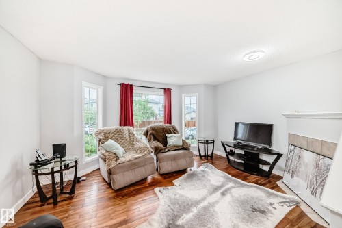 Living area featuring wood-finish flooring, light neutral wall paint, and a bay window with multiple panes - 8 Campbell Court, Leduc, AB 