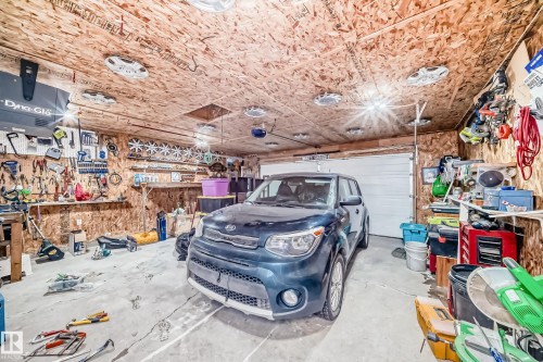 Garage space featuring a single overhead door, exposed OSB walls and ceiling, and multiple ceiling-mounted light fixtures - 8 Campbell Court, Leduc, AB 