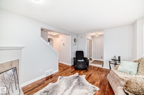 Hardwood-finish flooring extending into the hallway and entryway, light neutral wall paint, and a tiled fireplace surround - 8 Campbell Court, Leduc, AB 