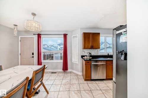 Dining area and kitchen featuring tile flooring, light grey wall paint, a kitchen with wood cabinetry, black countertops, and a stainless steel dishwasher - 8 Campbell Court, Leduc, AB 