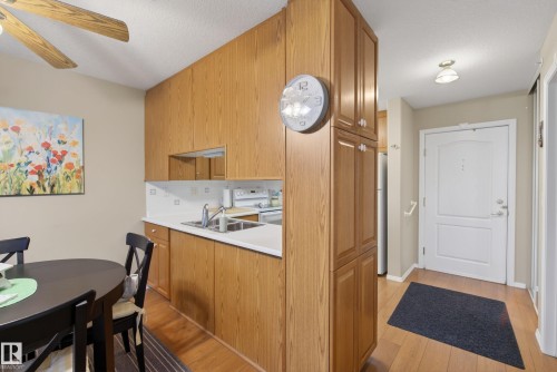 Kitchen and entryway area featuring wood-finish cabinetry, white countertops, and stainless steel sink - 413 8912 156 Street Nw, Edmonton, AB 
