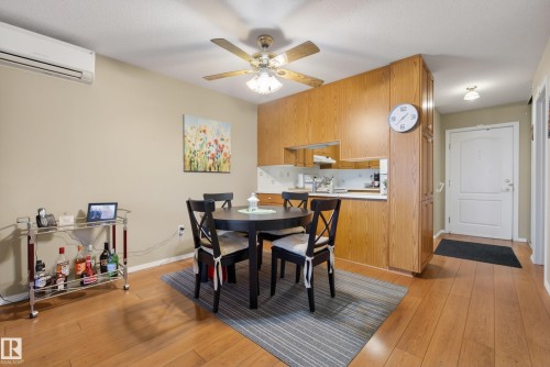 Dining area featuring wood-finish flooring, a ceiling fan with integrated lighting, and a wall-mounted air conditioning unit - 413 8912 156 Street Nw, Edmonton, AB 