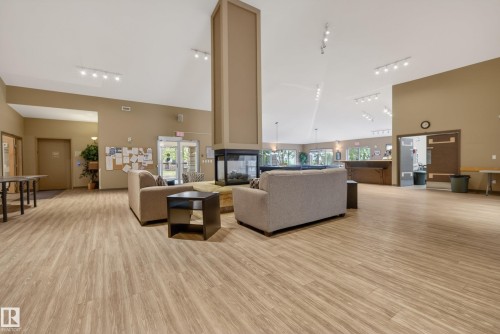 Spacious common area featuring vaulted ceilings, wood-finish flooring, a central three-sided fireplace, recessed lighting, and multiple windows - 413 8912 156 Street Nw, Edmonton, AB 