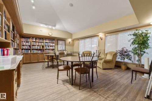 Spacious room featuring extensive built-in wood cabinetry and shelving, light wood-finish flooring, recessed lighting, and large windows with privacy coverings - 413 8912 156 Street Nw, Edmonton, AB 