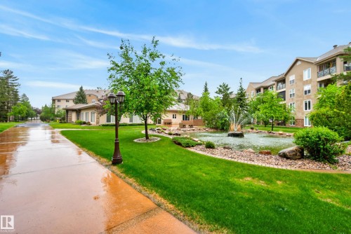 Manicured common grounds featuring a prominent water fountain in a rock-lined pond, surrounded by lush green lawns and mature trees - 413 8912 156 Street Nw, Edmonton, AB 