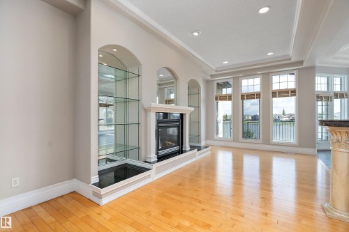 Open concept living space featuring a built-in fireplace with a stone surround, arched display alcoves with glass shelving and mirrored backing, light wood-finish flooring, recessed lighting, and a coffered ceiling - 16103 89 Street, Edmonton, AB - Indoor With Fireplace