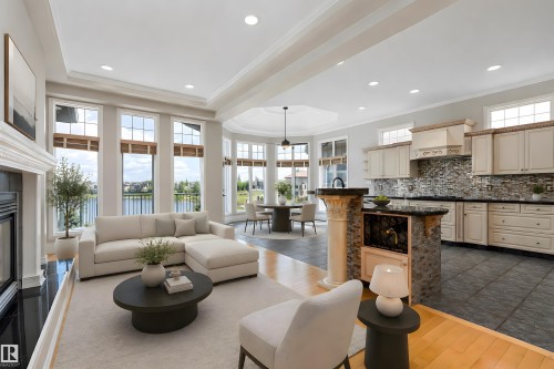 Spacious interior with an open layout, featuring a fireplace with a dark stone hearth, crown molding, a kitchen with cabinetry, and an island with a built-in wine rack - 16103 89 Street, Edmonton, AB - Indoor