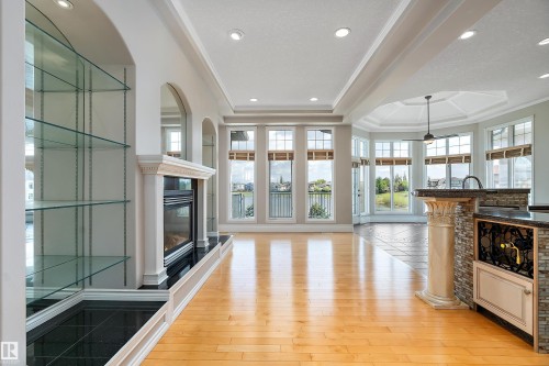 Open-concept interior featuring light wood-finish flooring, a built-in fireplace with black tile surround, and expansive windows - 16103 89 Street, Edmonton, AB - Indoor With Fireplace